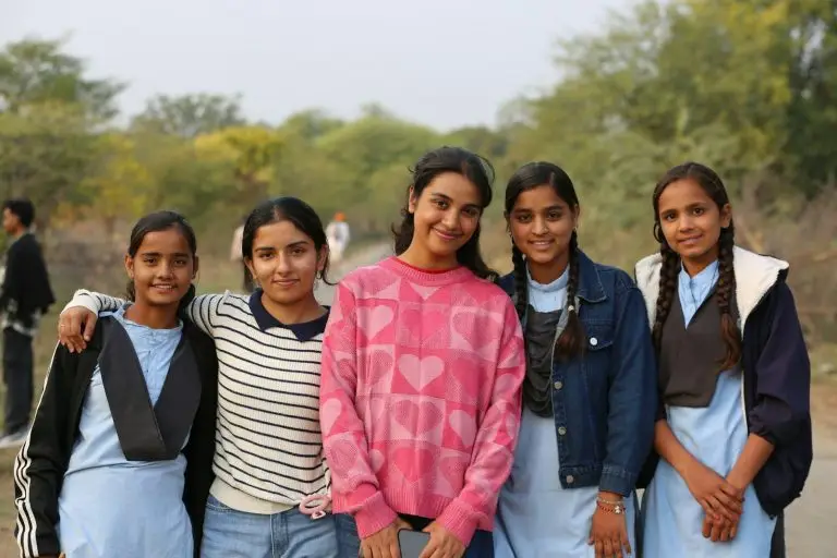 Five smiling girls stand together outdoors.
